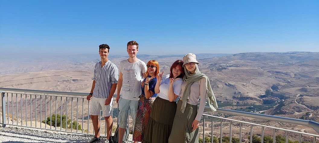 Im Bild zu sehen sind fünf Teilnehmer_Innen der Lehrgrabung (Szabolcs Gal, Michael Strebl, Carlotta Wilhelmi, Katharina Göschelbauer und Amal Ahmed) bei einem Ausflug auf Mount Nebo, vor der malerischen Landschaft Jordaniens.
